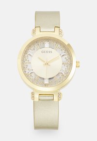 Goldfarbene Uhr mit rundem Gehäuse, beigem Glitzerdial und grünem Metallic-Armband. Mit Kristallakzenten auf der Lünette und den Stundenmarkierungen.