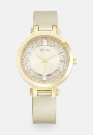 Goldfarbene Uhr mit rundem Gehäuse, beigem Glitzerdial und grünem Metallic-Armband. Mit Kristallakzenten auf der Lünette und den Stundenmarkierungen.