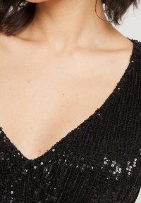 Svart ärmlös topp med en djup V-ringning, förskönad med paljetter som skapar en texturerad, reflexiv yta.