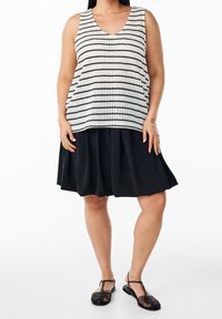 Černobílý pruhovaný tílkový top z pletené tkaniny. Kombinován s černou plisovanou sukní po kolena a černými sandály s pásky.