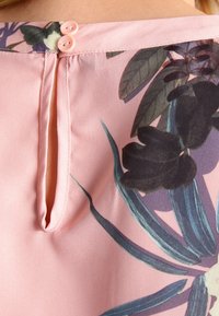 Blusa rosa pallido con stampa floreale, apertura a occhiello sulla schiena e due piccoli bottoni rosa per la chiusura. Tessuto dalla consistenza liscia.