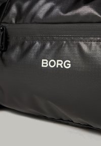 Melnā neilona soma ar tekstūrētu virsmu, kas izceļas ar izteiksmīgu baltu "BORG" logo un rāvējslēdzēja aizdari. Vienkāršs dizains ar elegantīgu izskatu.