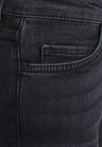 Vaqueros de denim negro con un diseño de cinco bolsillos, textura sutil y detalle de costura a lo largo de las costuras. Corte ajustado con un aspecto moderno.