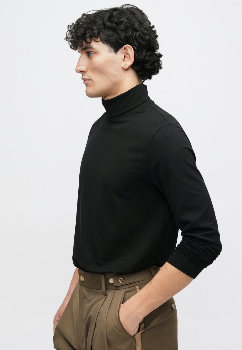 Sort turtleneck skjorte i et glat stof, med lange ærmer og et tætsiddende design, parret med beige høj talje bukser.