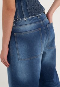Džínové kalhoty v bledě modré barvě s širokým střihem nohavic, dvěma zadními kapsami, viditelným šitím a třepeným lemováním.