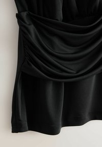 Zwarte jersey top met gedrapeerde stof bij de taille, een gladde textuur en een losse pasvorm met een ronde zoom. Naaddetails zichtbaar.
