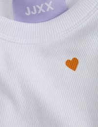 Valge ribadega kangast särk, millel on rinnal väike oranž süda, ja kaeluse lähedal on lilla silt, millel on kirjas "JJXX".