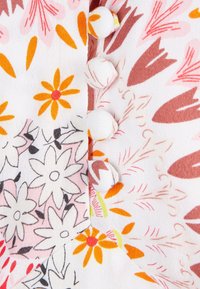 Tessuto bianco con motivi floreali multicolori in arancione, rosa e nero, con tre bottoni rivestiti di tessuto lungo il lato.