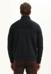 Zwarte sportjack met ribbeldetails op de schouders, lange mouwen en een hoge kraag. Gladde textuur en nauwsluitend ontwerp.