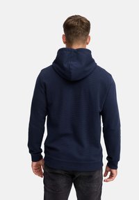 Navy blue hoodie with a textured fabric, featuring a large, adjustable hood and a ribbed hem. Back view reveals long sleeves and simple design.