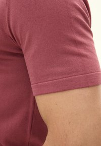 T-shirt a maniche corte di colore bordeaux, realizzato con un tessuto leggero, caratterizzato da una texture liscia e orli delle maniche rifiniti con cura.