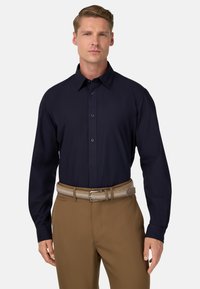 Námořnická košile s dlouhým rukávem a límečkem na knoflíky, hladká textura a zapínání na knoflíky vepředu, doplněná o světle hnědé kalhoty a pletený pás.