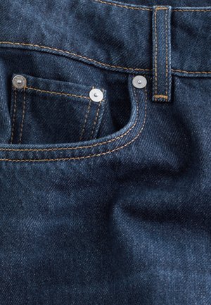 Dark blue denim jeans with copper stitching, featuring a small front pocket and silver hardware. Texture is smooth with a slight sheen.