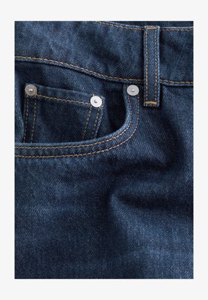 Dunkelblaue Jeans aus Denim mit kupferfarbener Nähte, ausgestattet mit einer kleinen Vordertasche und silbernem Zubehör. Die Textur ist glatt mit einem leichten Glanz.