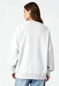 Világosszürke pulóver laza szabással, raglán ujjakkal és bordázott mandzsettákkal. Puha anyagból készült, sima tapintású.