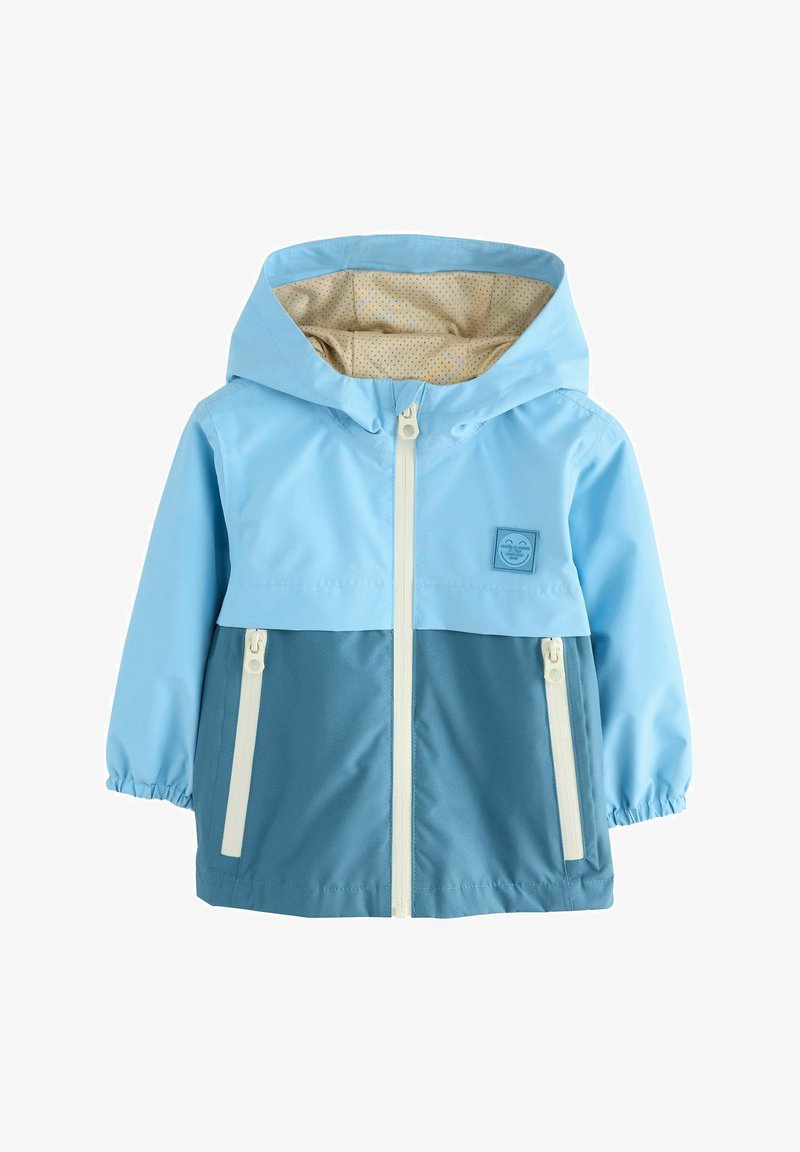 Giacca da pioggia blu chiaro e blu scuro con cappuccio, caratterizzata da zip bianche e una fodera a pois. Include un emblema sul petto.