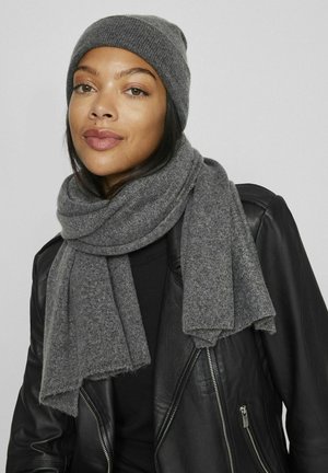 Gray knit beanie and matching scarf made of soft, textured fabric. Scarf drapes around the neck, complemented by a black leather jacket.