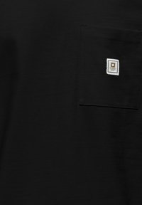 Zwarte T-shirt gemaakt van zacht materiaal, met een borstzakje met een vierkante label, gestikte randen en een gladde textuur.