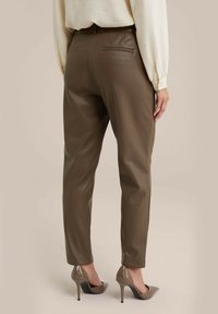 Bruine nep leren tapered broek met zijzakken en achterste paspelzakken, gecombineerd met een beige blouse met lange mouwen en nude hoge hakken.