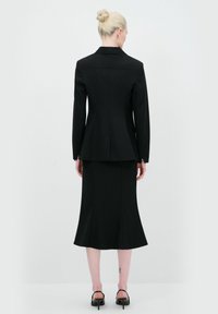Completo nero su misura con giacca aderente e gonna svasata. Tessuto liscio, rever affilati e dettagli sui polsini. Design semplice ed elegante.