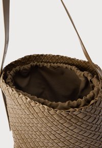 Heledast beežist punutud nahast kott pehme kangast tõmbenööriga sees. Varustatud pika, lameda õlarihmaga.