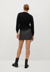 Pull noir, mini-jupe grise scintillante, bottines noires. Tissu lisse du pull, jupe ajustée et texturée, semelles épaisses des bottines. Fond uni.
