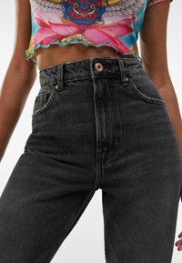 Džínové kalhoty s vysokým pasem, černé barvy, s mírně vybledlou texturou. Mají pět kapes a malý kovový knoflík na pasu.