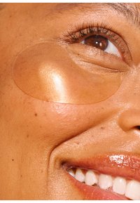 Patch oculaire en hydrogel sur la peau sous l'œil, transparent avec un subtil éclat. Texture lisse contre un teint chaud et radieux.
