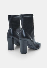 Botas de cuero negras hasta el tobillo con un diseño elegante, punta afilada y tacón grueso. Presentan un acabado suave y detalles de costura mínimos.