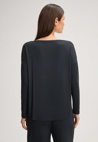 Czarna bluzka z długim rękawem, luźny krój, okrągły dekolt, miękka faktura, delikatny połysk, z opuszczonymi ramionami i prostym dołem.