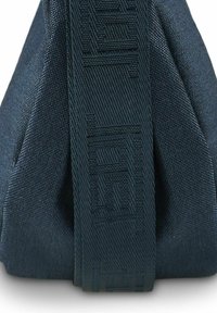 Bolsa de tela azul oscuro con un acabado texturizado. Presenta una correa tejida prominente con letras en relieve y una forma angular.