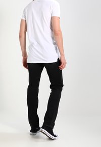 Jeans negros de corte slim y diseño de pierna recta. Combinados con una camiseta blanca básica y zapatillas negras de estilo bajo.
