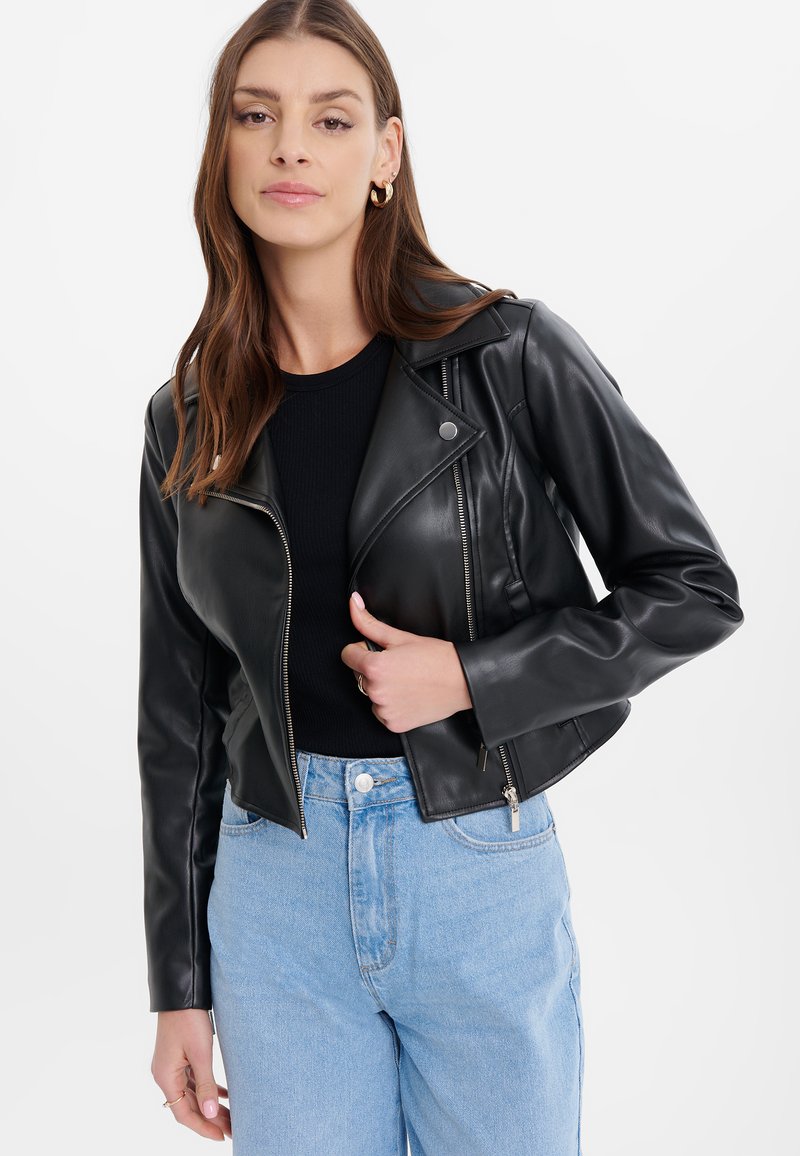 Giacca moto in pelle nera con un design aderente, cerniere sul davanti e ai polsini, colletto con revers, abbinata a jeans azzurri chiari.