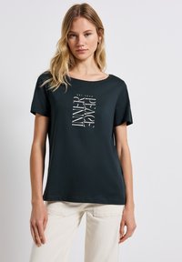 T-shirt en coton noir à manches courtes et col rond, présentant un design de texte blanc qui indique « TROUVEZ VOTRE PAIX INTÉRIEURE » verticalement.