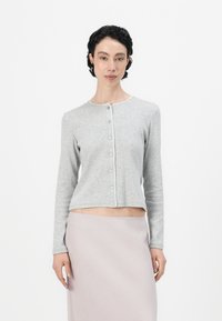 Lys grå cardigan med lange ermer, rund halslinje og knappelukking foran. Har en cropped passform og subtil ribbestrikket tekstur.