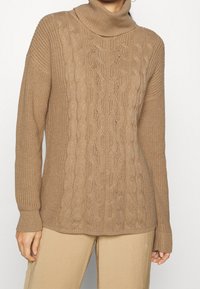 Beige gebreide trui met een omgeslagen col, voorzien van een getextureerd kabelpatroon in het midden en geribde manchetten. Glad, zacht materiaal.