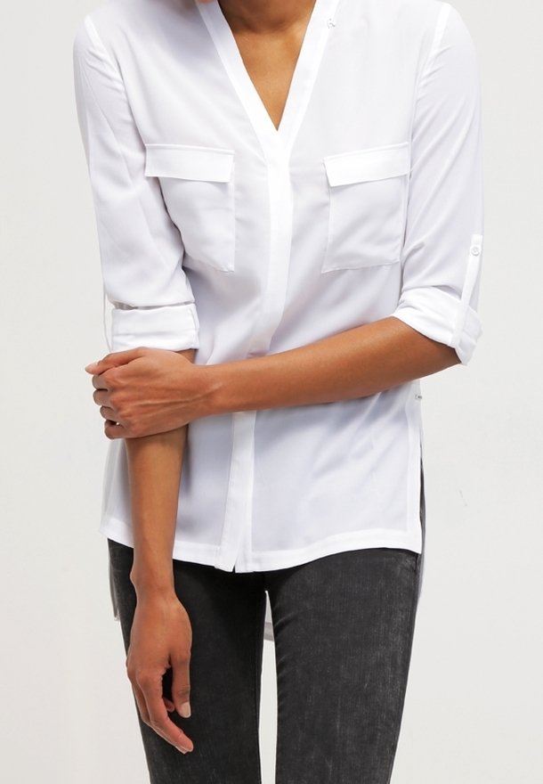 Vit skjorta med V-ringning, som har två bröstfickor, uppvikta ärmar, sido-slitsar och ett mjukt, lätt tyg.