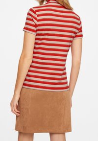 Camisa polo de manga corta a rayas en rojo y beige, con un diseño ajustado y textura suave, combinada con una falda de ante color marrón.