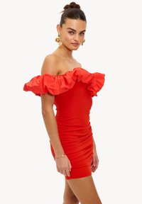 Robe rouge à épaules dénudées avec un col volanté évasé, un corsage cintré et une texture froncée. Longueur courte avec un tissu lisse.