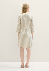 Robe courte beige à rayures, avec une taille cintrée, des manches trois-quarts et un ourlet droit. Le tissu semble léger et lisse.