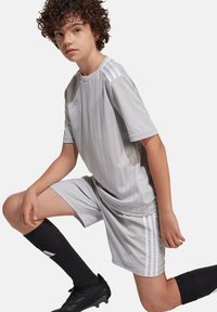 Grijze sportjersey met korte mouwen en subtiele verticale strepen, gecombineerd met bijpassende korte broek, zwarte kniekousen en voetbalschoenen.