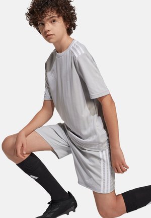 Grijze sportjersey met korte mouwen en subtiele verticale strepen, gecombineerd met bijpassende korte broek, zwarte kniekousen en voetbalschoenen.