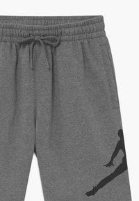 Graue Sweatpants mit elastischem Bund und verstellbarem Kordelzug. Mit schwarzem Silhouetten-Graphic am Unterschenkel und seitlichen Taschen.