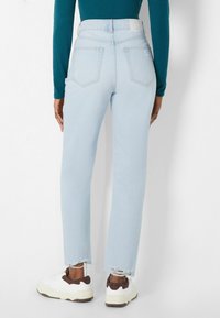 Vaaleansiniset korkeavyötäröiset farkut, joissa on suora lahje, repaleinen helma, takataskut ja etiketti vyötärönauhassa. Yhdistettynä valkoisiin lenkkareihin.