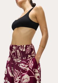 Top corto nero a costine abbinato a pantaloni largo con motivo floreale bordeaux, dotati di una vita arricciata e tasche laterali. Bracciale dorato al polso.