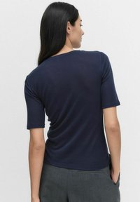 Laivansininen t-paita lyhyillä hihoilla ja pyöreällä kaula-aukolla; sileä kangas, jossa on hieman venyvyyttä, ja siinä on kaareva takahasim ja yksinkertainen muotoilu.