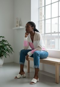 Sweter dzianinowy w różowe, kremowe i beżowe paski, z zapięciem na guziki i żebrowanymi mankietami. W połączeniu z jasnoniebieskimi dżinsami i białymi klockowymi pantoflami.