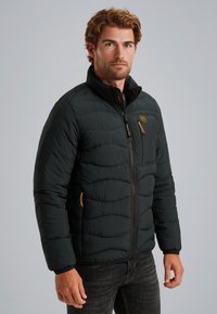 Crna puffer jakna s patentnim zatvaračem sprijeda, rebrastim manžetama i svijetlo narančastim naglascima. Tekstura je quilted za dodatnu izolaciju.