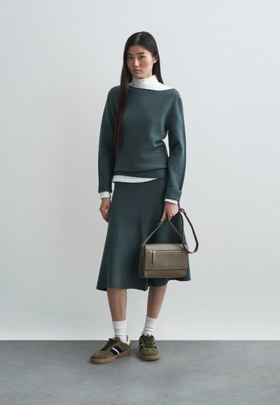 Σκούρο πράσινο πουλόβερ και φούστα από υφασμάτινη υφή, συνδυασμένα με ελιών sneakers, λευκές κάλτσες και καφέ τσάντα ώμου.