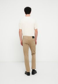 Μπεζ chinos με πίσω τσέπες, συνδυασμένα με ένα ανοιχτό κρεμ μπλουζάκι. Λείο ύφασμα; σχεδιασμός με ίσια μπατζάκια; φορεμένα με μαύρα παπούτσια.